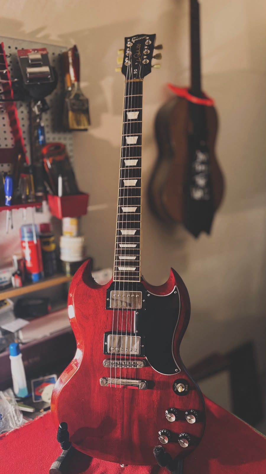 Guitarra eléctrica en el atril del taller, con el tablero de herramientas de fondo